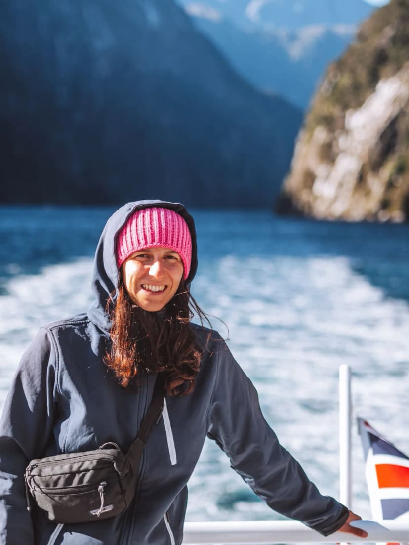 IMMAGINE DI UNA RAGAZZA CHE GUARDA IN CAMERA SULLA BARCA DELLA CROCIERA PANORAMICA A MILFORD SOUND CON SULLO SFONDO IL FIORDO