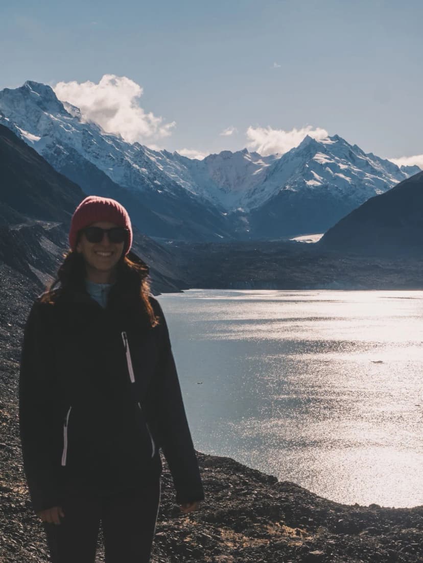 Escursionista con il viso rivolto verso la camera che sorride, sullo sfondo il lago e il Mount cook innevato