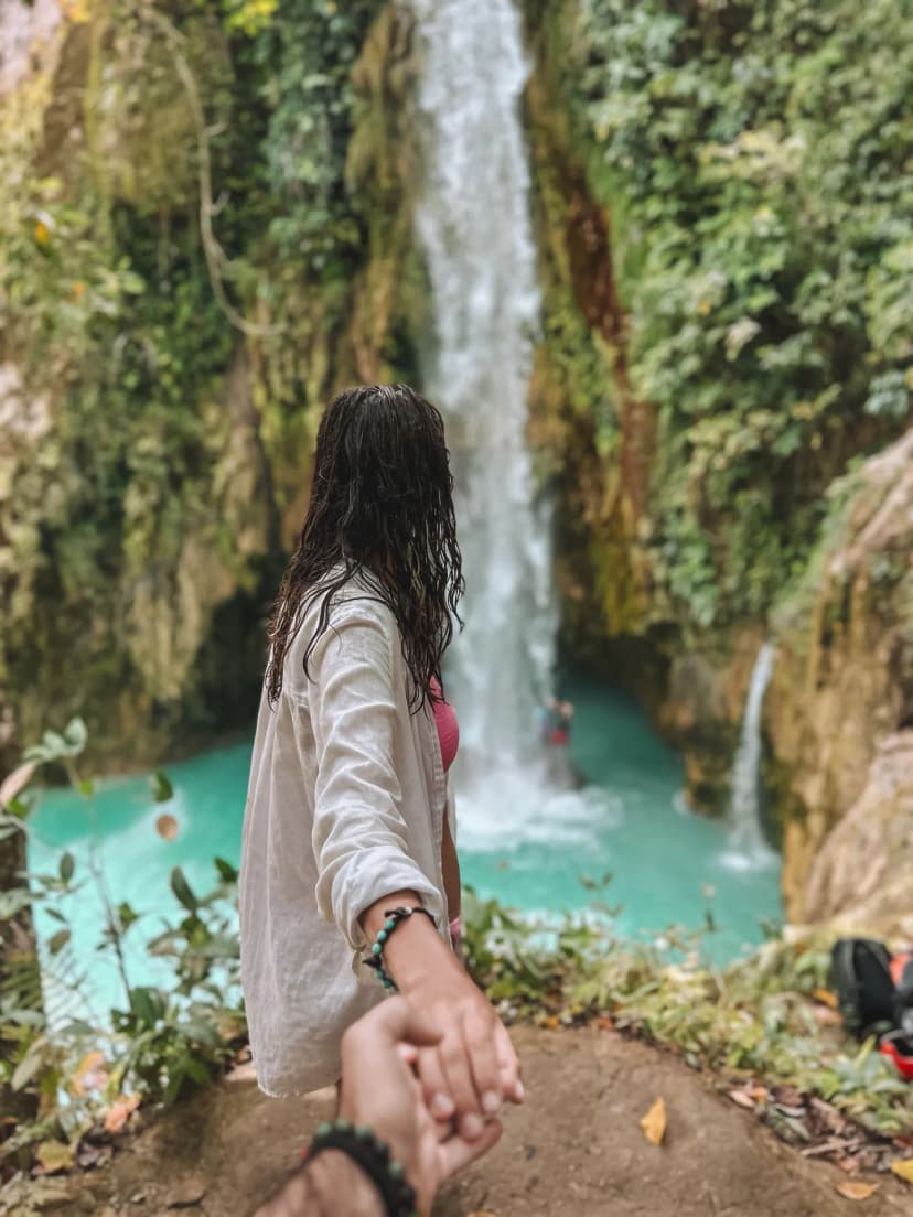 ragazza di spalle che tende la mano verlo la camera e sullo sfondo la cascata di Moalbol
